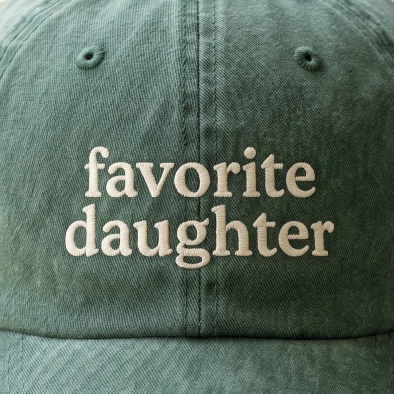 Pode incluir: Bon&eacute; de beisebol verde com o texto bordado "favorite daughter" em branco. O bon&eacute; tem uma aba curva e um design cl&aacute;ssico de seis pain&eacute;is. O tecido tem uma apar&ecirc;ncia ligeiramente desbotada.