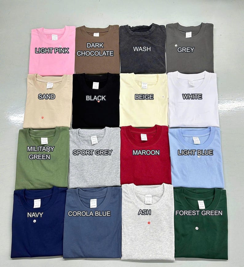 Puede incluir: Una cuadr&iacute;cula de camisetas dobladas en varios colores, incluyendo rosa claro, chocolate oscuro, gris, arena, negro, beige, blanco, verde militar, gris deportivo, granate, azul claro, azul marino, azul corola, ceniza y verde bosque. Cada camiseta tiene una etiqueta y el nombre del color.