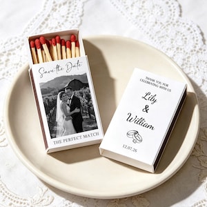 May include: Two rectangular matchboxes with red-tipped wooden matches. One box is open, showing a black-and-white photo of a couple, the text Save the Date and THE PERFECT MATCH. The other box features the text Lily & William, 12.07.26, and rings.