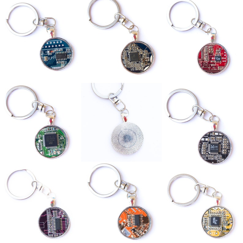 May include: A collection of round keychains featuring circuit board designs in various colors. Each keychain has a silver-tone metal ring and chain. The circuit boards display intricate electronic components and come in colors like blue, red, green, and orange.