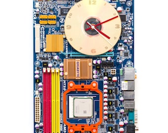 May include: A clock constructed from a blue computer motherboard. The clock face is a gold disc with black numerals and red hands. Various computer components, including gold and orange heatsinks, are visible. The text "GIGABYTE" is printed on the motherboard.
