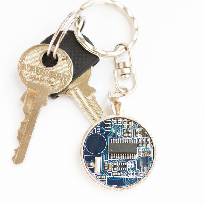 May include: A silver keychain with two keys and a round pendant. The pendant features a blue circuit board design with a silver border. One key is stamped "MADE IN CHINA".