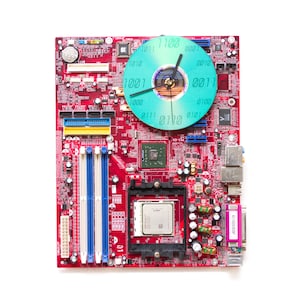 May include: A red computer motherboard with a blue and green clock face on top. The clock face has binary code numbers around the edge.