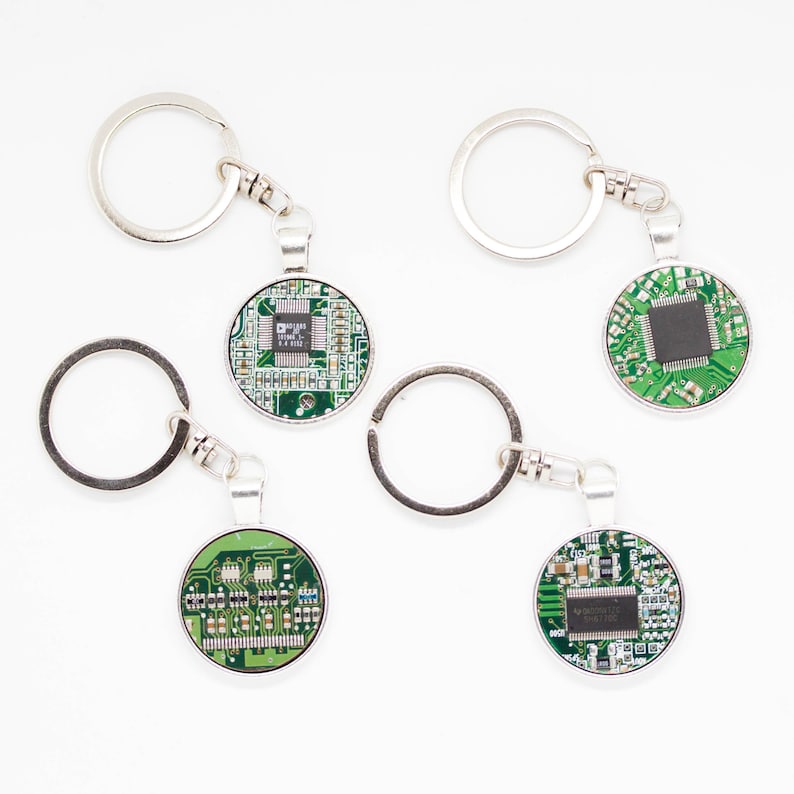 May include: Keychains with a round, silver-toned pendant featuring a green circuit board design. Each keychain has a silver key ring and clasp. The circuit board designs vary slightly, showcasing different electronic components.