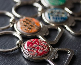 May include: Several silver bottle openers with circular, colourful circuit board designs. Each opener has a key ring. The circuit board designs are red, orange, green, and blue.