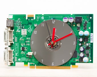 May include: A green circuit board with a silver clock face and red hands. The clock face has black numbers 1 through 12. The circuit board has the text "NVIDIA" and "VET" printed on it.