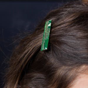 May include: A green and white circuit board hair clip. The rectangular clip is inserted into brown hair, with the electronic components visible. The clip adds a unique, tech-inspired accent to the hairstyle.