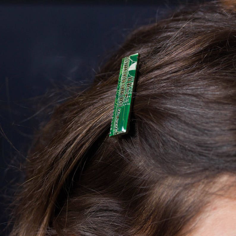 May include: A green and white circuit board hair clip. The rectangular clip is inserted into brown hair, with the electronic components visible. The clip adds a unique, tech-inspired accent to the hairstyle.