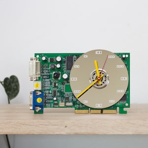 Op de afbeelding: Een unieke klok gemaakt van een groene printplaat met een goudkleurige wijzerplaat. De wijzers zijn geel en rood. De klok is een creatief stukje tech-geïnspireerde decoratie.