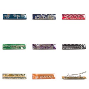 May include: Nine rectangular circuit boards in various colors, including green, red, and purple, are arranged on a white background. Each board displays intricate electronic components and patterns. One board has a silver metal clip attached.