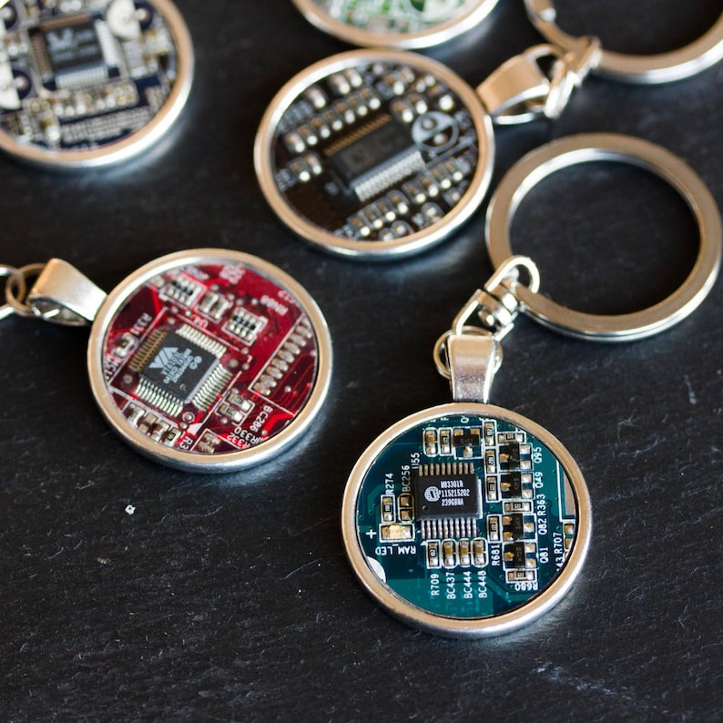 May include: Circular keychains featuring colorful circuit board designs. Each keychain has a silver-toned metal frame and a key ring. The circuit boards are red, green, and black, with various electronic components.
