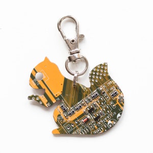 May include: A unique squirrel-shaped keychain made from recycled circuit board material. The keychain features a silver-colored clasp and a detailed design with green and orange hues, showcasing electronic components.