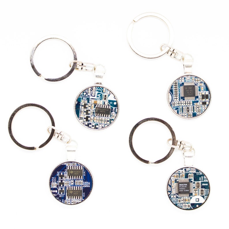 May include: Four keychains with round, blue circuit board pendants. Each pendant has a silver-colored metal frame and a silver keyring. The circuit boards have white and silver components.