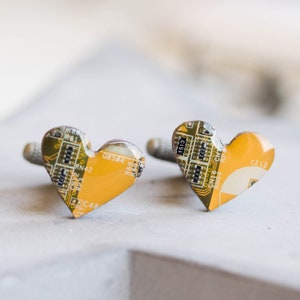 Könnte beinhalten: Herzförmige Manschettenknöpfe aus recycelten Leiterplatten. Die Manschettenknöpfe haben ein gelb-grünes Farbschema mit sichtbaren elektronischen Bauteilen. Ein einzigartiges Accessoire für Technikbegeisterte.