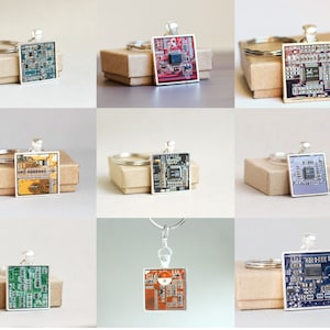May include: A collection of square silver keychains featuring colorful circuit board designs. Each keychain has a different color scheme, including green, red, blue, and orange. The keychains are displayed on small, brown cardboard boxes.