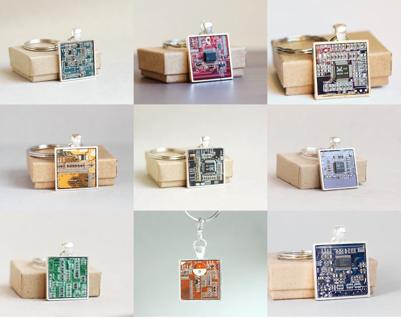 May include: A collection of square silver keychains featuring colorful circuit board designs. Each keychain has a different color scheme, including green, red, blue, and orange. The keychains are displayed on small, brown cardboard boxes.