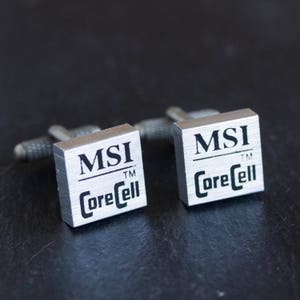 Peut inclure: Une paire de boutons de manchette en argent avec le logo MSI et le texte "CoreCell" en lettres noires.