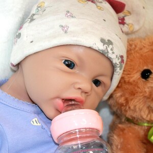 A baby doll is positioned on a blanket with a teddy bear, symbolizing innocence and the joy of playtime.