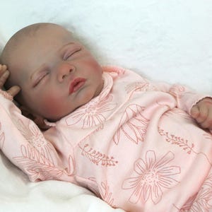 A baby doll peacefully sleeps, dressed in a soft pink outfit, exuding a sense of calm and innocence.