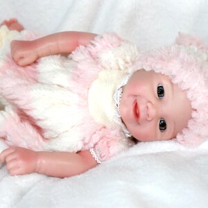 A cute baby doll wearing pink attire and a hat, positioned on a light background.