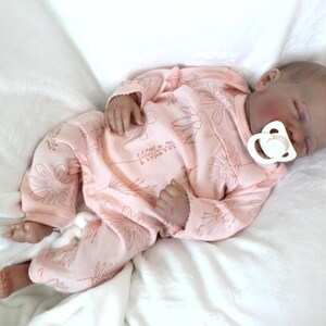 A baby doll peacefully sleeps, dressed in a soft pink outfit, exuding a sense of calm and innocence.