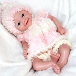 A cute baby doll wearing pink attire and a hat, positioned on a light background.