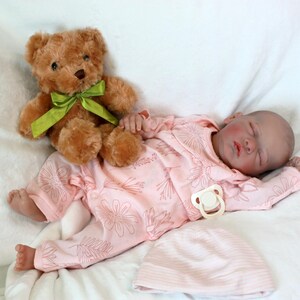 A baby doll peacefully sleeps, dressed in a soft pink outfit, exuding a sense of calm and innocence.