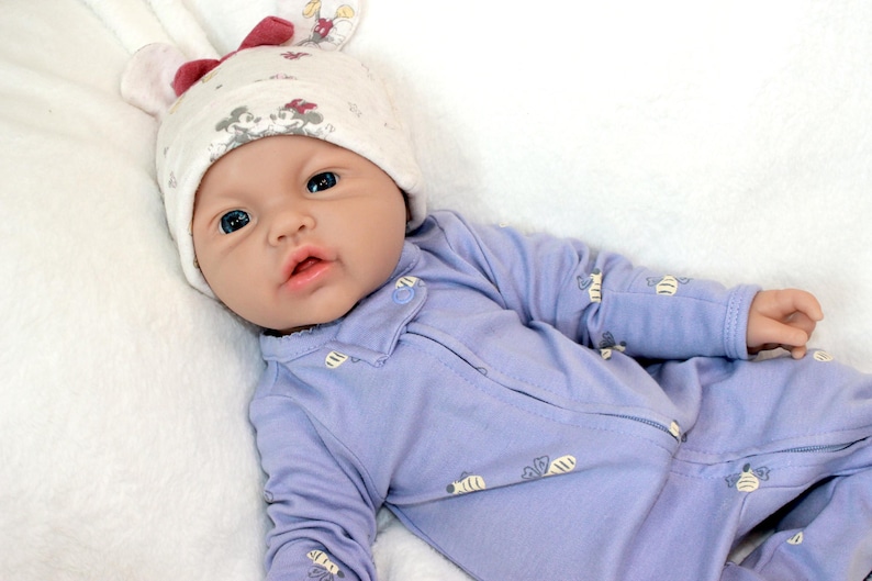 A baby doll resting on a soft white blanket, showcasing its delicate features and clothing.