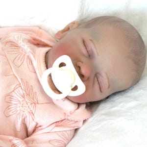 A baby doll, adorned in a pink outfit, is soundly sleeping, radiating a gentle and soothing presence.