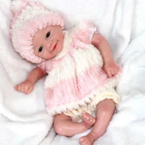 A cute baby doll wearing pink attire and a hat, positioned on a light background.