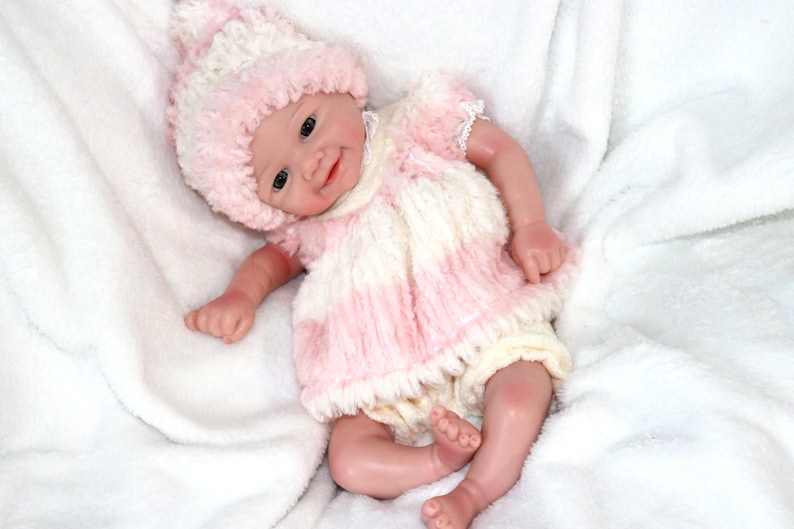 A cute baby doll wearing pink attire and a hat, positioned on a light background.