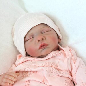 A serene baby doll in a pink outfit is sleeping, embodying tranquility and charm in its delicate appearance.