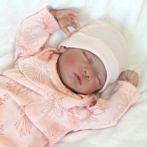 A baby doll, adorned in a pink outfit, is soundly sleeping, radiating a gentle and soothing presence.