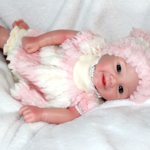 A cute baby doll wearing pink attire and a hat, positioned on a light background.