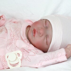 A serene baby doll in a pink outfit is sleeping, embodying tranquility and charm in its delicate appearance.