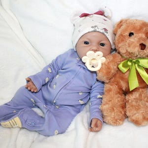 A baby doll lies on a colorful blanket next to a teddy bear, evoking a sense of warmth and childhood comfort.
