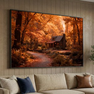 Könnte beinhalten: Gerahmter Leinwanddruck, der eine Hütte in einem herbstlichen Wald zeigt. Das Bild zeigt einen Weg, der zu der Hütte führt, umgeben von Bäumen mit orangefarbenen und roten Blättern. Rauch steigt aus dem Schornstein auf und erzeugt eine warme und einladende Szene.