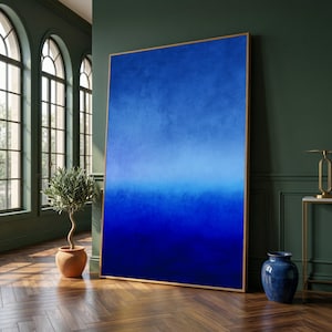 Puede incluir: Gran obra de arte abstracta enmarcada con un degradado de azules, de claro a índigo profundo. La obra de arte se exhibe en una habitación con una pared verde oscuro, una planta en maceta y un jarrón azul. El marco es de color madera clara.