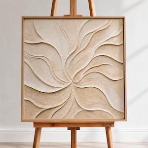 May include: A square, beige abstract art piece with a swirling, textured design, framed in a light brown wooden frame. The artwork is displayed on a wooden easel, showcasing its neutral tones and organic shapes.