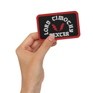 May include: A black and red embroidered patch with the text "Lord Timothy Dexter" in white lettering and a red lightning bolt symbol.