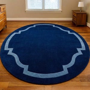 May include: A large circular area rug featuring a deep navy blue center and a lighter blue border with a quatrefoil-inspired geometric outline. The rug has a solid color field and a clean, simple design that covers a portion of the wooden floor.