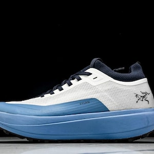 May include: A blue and white athletic shoe with the word "SYLAN" printed on the side. The shoe has a thick, light blue sole and a mesh upper. A black logo is on the side of the shoe.