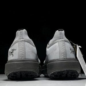 Puede incluir: Par de zapatillas deportivas grises con suela gris oscuro, vistas desde atr&aacute;s. Las zapatillas tienen una parte superior texturizada y un peque&ntilde;o logotipo en el lateral. Una etiqueta cuelga de una zapatilla.