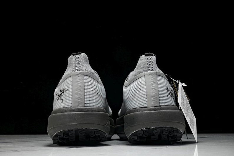 Puede incluir: Par de zapatillas deportivas grises con suela gris oscuro, vistas desde atr&aacute;s. Las zapatillas tienen una parte superior texturizada y un peque&ntilde;o logotipo en el lateral. Una etiqueta cuelga de una zapatilla.