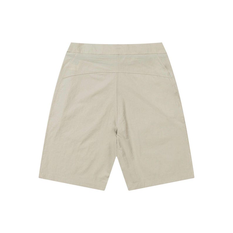 May include: A pair of beige shorts. The shorts have a high waist and a relaxed fit, with a visible seam down the center of the front and back. The fabric appears to be lightweight and slightly textured, suitable for warm weather.