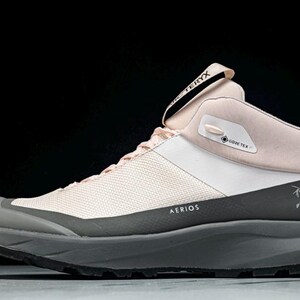 May include: A light pink and white hiking boot with a gray sole. The boot features the text "AERIOS" and "GORE-TEX". The brand name "ARC'TERYX" is visible on the tongue. A stylized logo is on the side.
