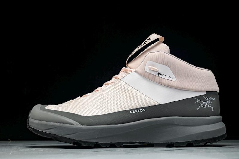 May include: A light pink and white hiking boot with a gray sole. The boot features the text "AERIOS" and "GORE-TEX". The brand name "ARC'TERYX" is visible on the tongue. A stylized logo is on the side.