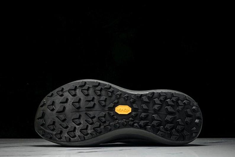 Puede incluir: Suela de zapatilla deportiva negra con un patr&oacute;n texturizado y un logotipo amarillo de Vibram. La suela est&aacute; dise&ntilde;ada para la tracci&oacute;n y la durabilidad, adecuada para actividades al aire libre. El calzado es probablemente para correr o caminar.