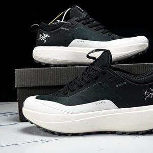 May include: Black and white athletic shoes with thick soles. The shoes have a black upper with white accents and a white sole. The brand logo is visible on the side. The word "SYLAN" is printed on the side of the shoe.