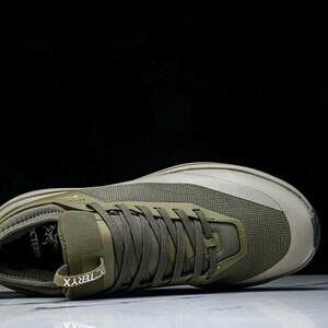 May include: Olive green athletic shoe with a mesh upper and a thick sole. The shoe features a lace-up closure and the brand name "Arc'teryx" is visible on the side. The shoe is designed for outdoor activities.